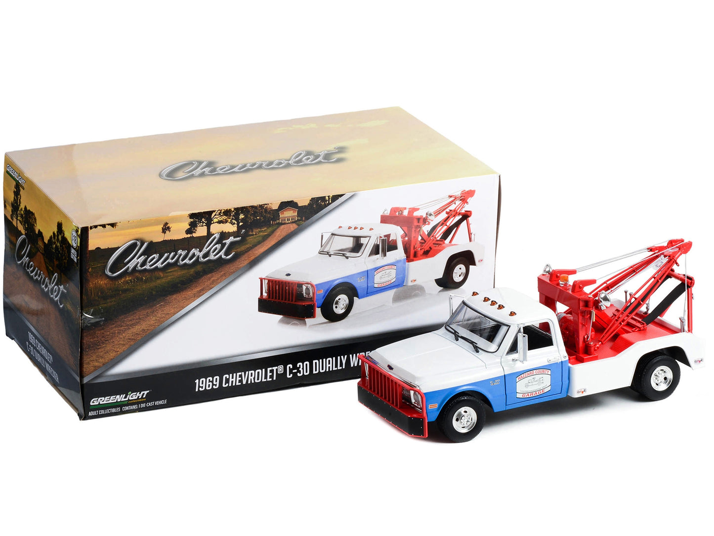 White and blue 1/18 scale diecast Chevrolet C-30 dually wrecker tow truck model by Greenlight, detailed with "Hazzard County Garage" branding.