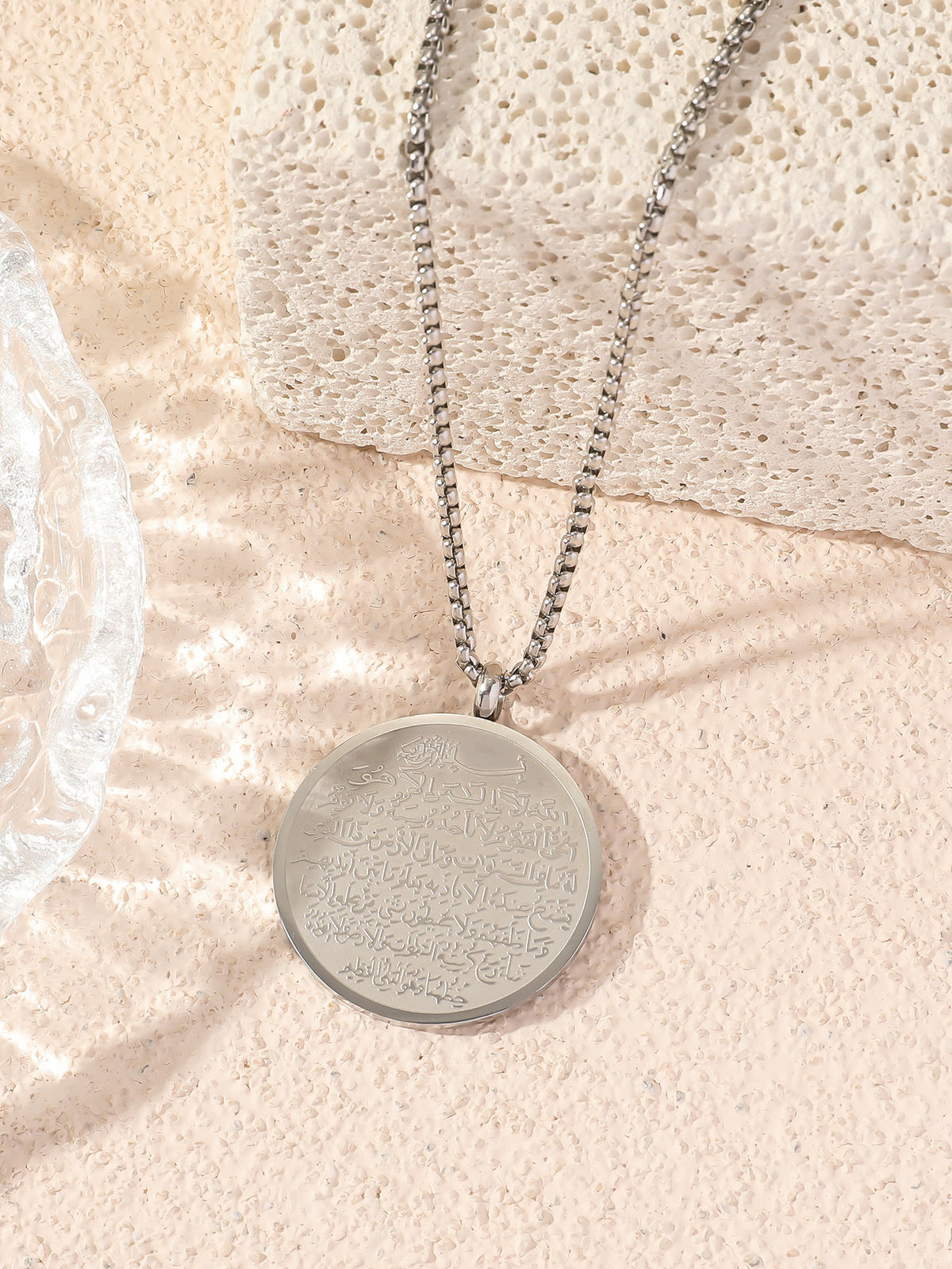 Round titanium Islamic pendant featuring Ayatul Kursi Quran inscription, worn as a religious Muslim necklace with medallion design.